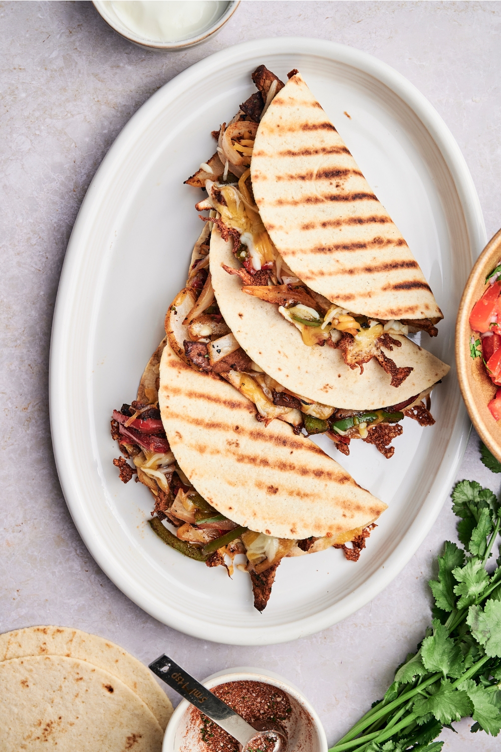 A white plate holds three grilled steak quesadillas. The quesadillas are full of steak, cheese and vegetables.
