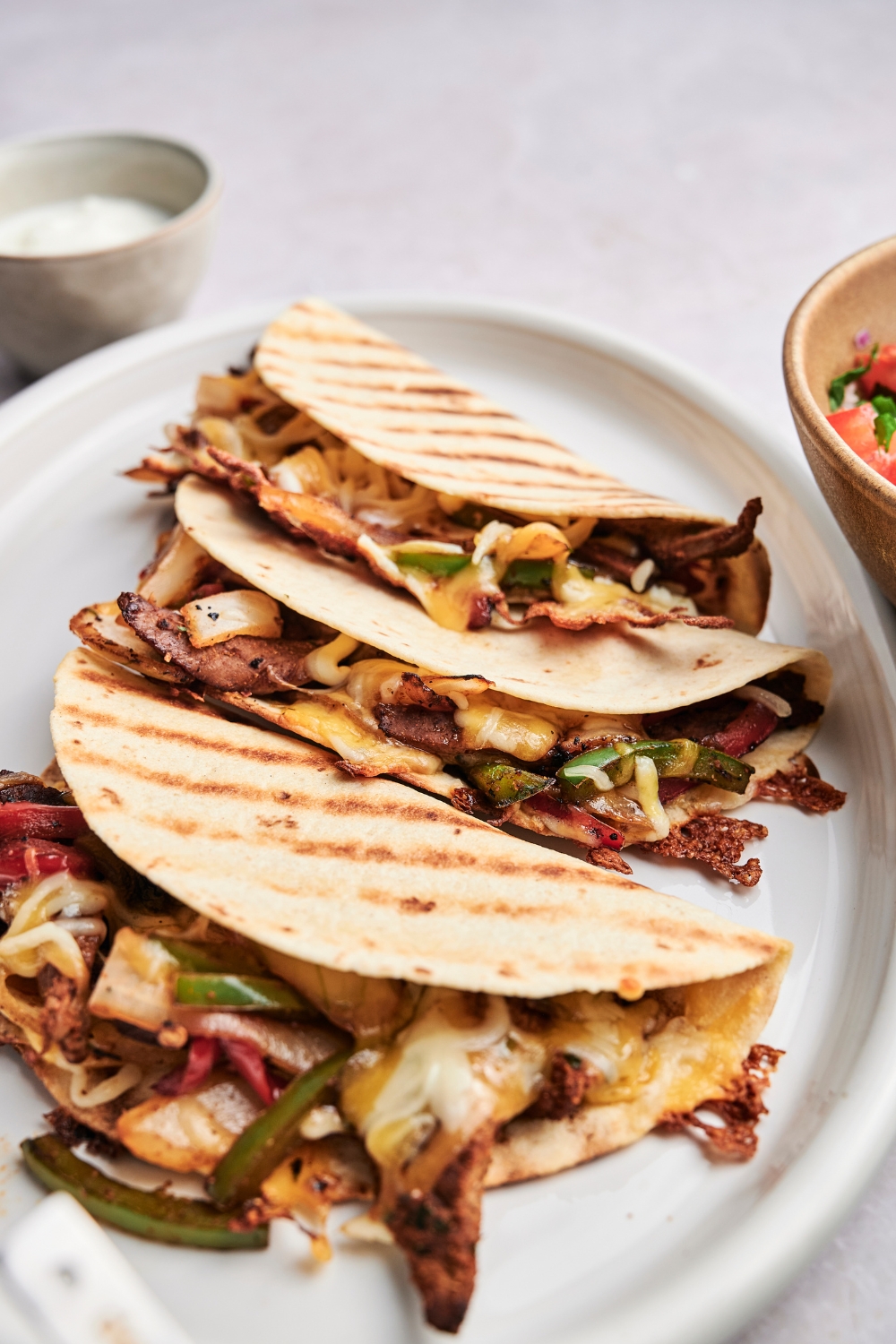 Three steak quesadillas are on a white serving platter. The quesadillas are stuffed full with steak and vegetables.