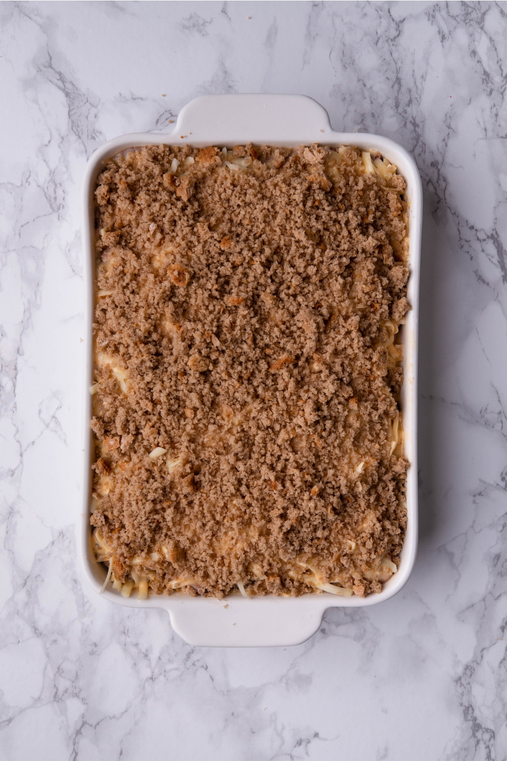 Unbaked Reuben casserole covered in bread crumbs in a white baking dish.