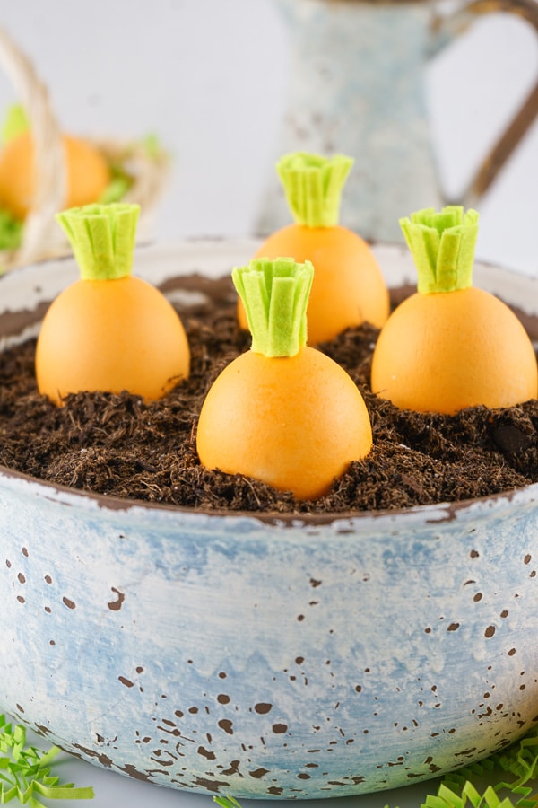 Easter eggs crafted to look like carrots in a pot with some dirt as a cute spring decoration.