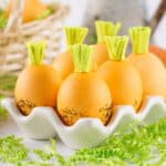 square crop of carrot Easter eggs in a white ceramic egg holder with green Easter grass around them.
