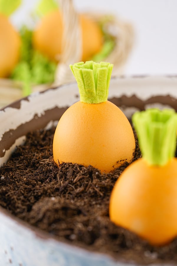 easter eggs dyed to look like carrots placed in a pot of dirt as a spring centerpiece.