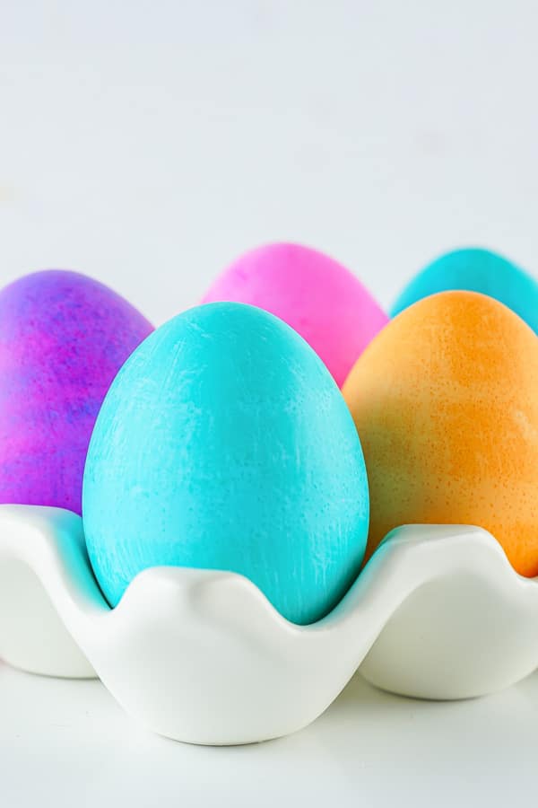 Colored Easter eggs in a white porcelain egg tray.