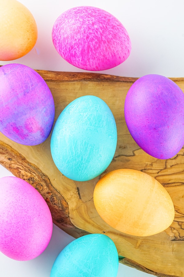 bright Easter eggs in blue, yellow, purple and pink on a wooden tray.