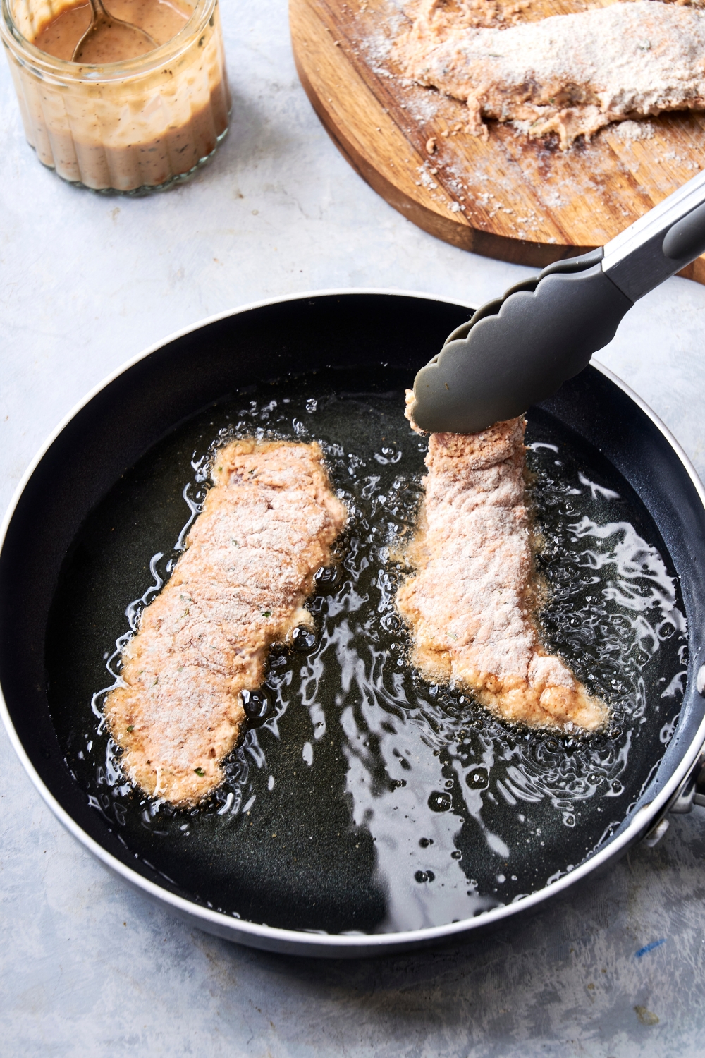 A frying pan with hot oil cooking the coated chicken tenders.