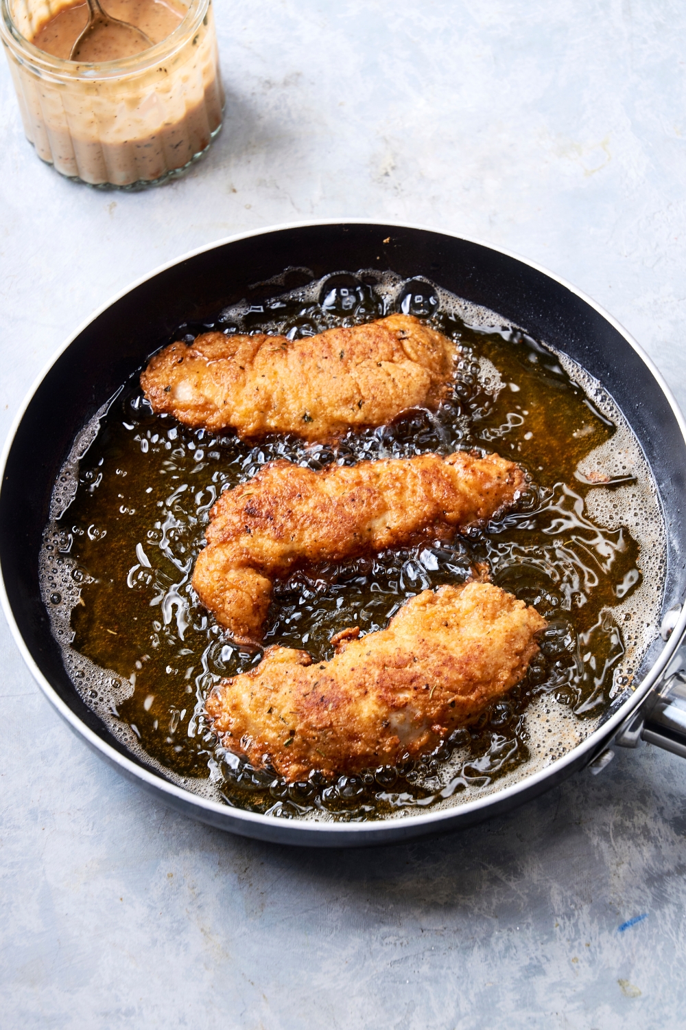 A frying pan with hot oil cooking the coated golden brown chicken tenders.