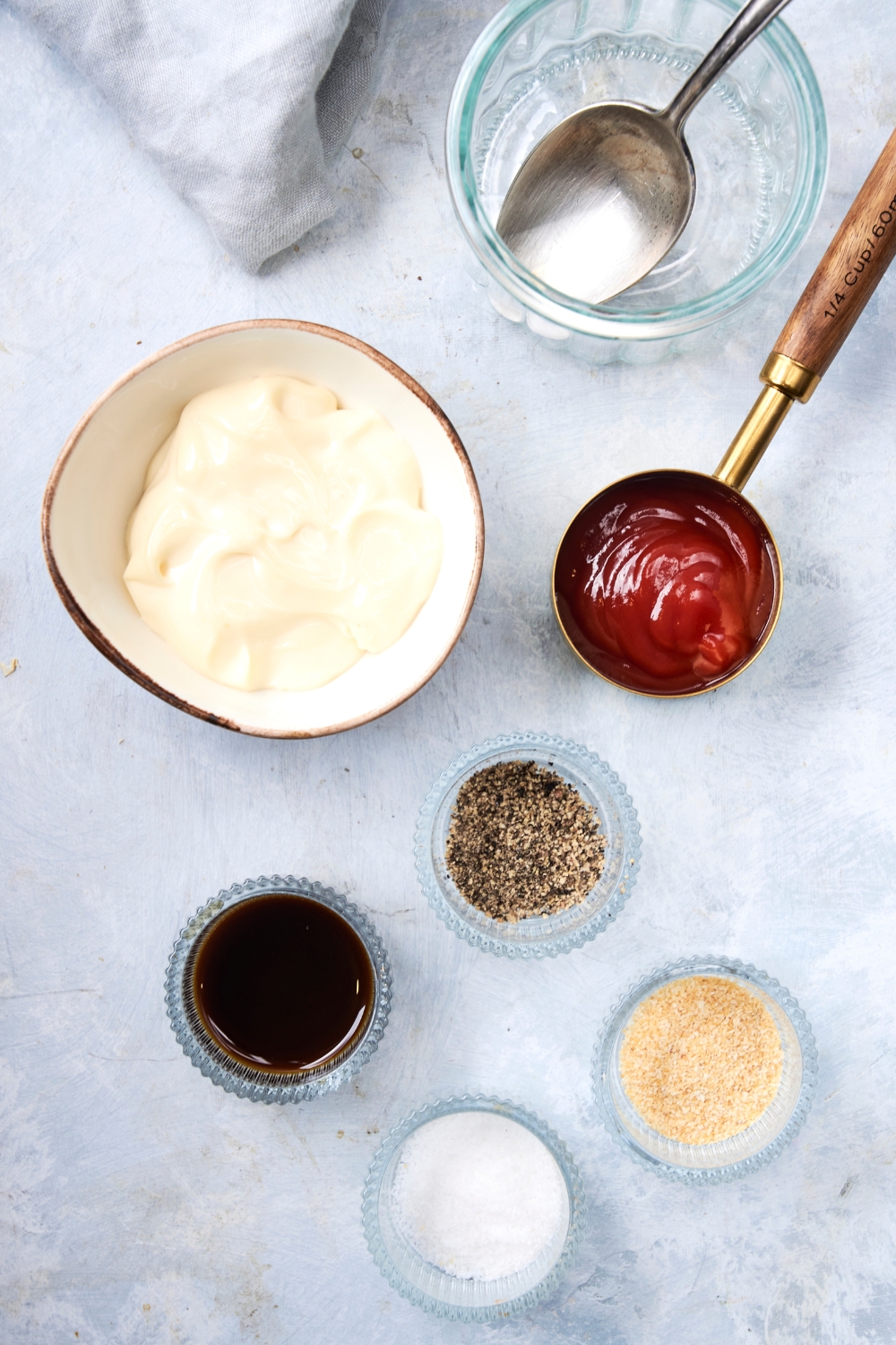 A countertop with various bowls with ingredients like mayo, ketchup, salt, pepper, Worcestershire sauce, and garlic powder.