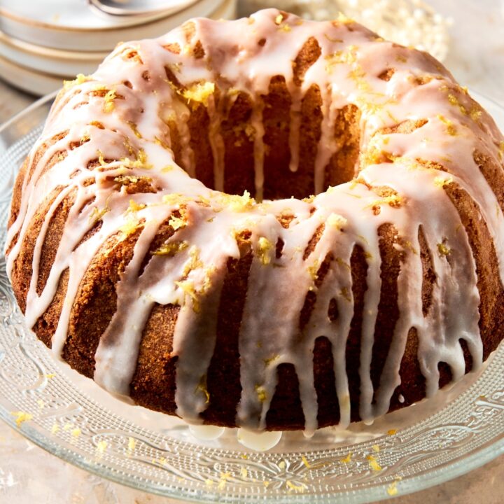 A cake tray with the lemon bundt cake on it iced with the lemon icing and garnished with extra lemon zest.