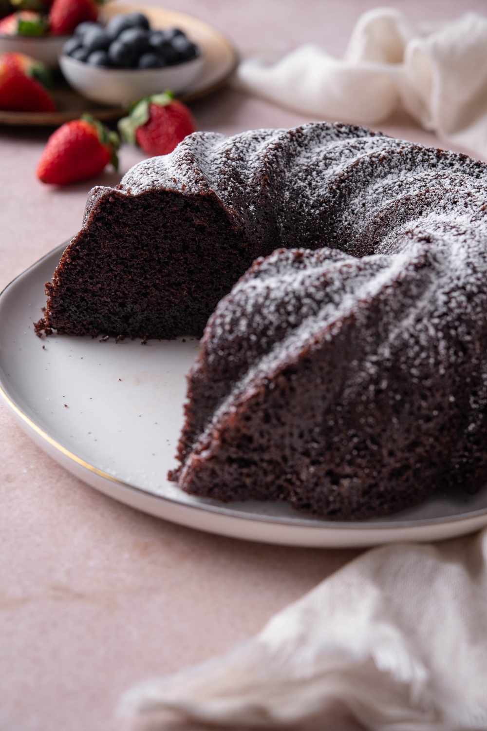 A whole chocolate pound cake sits on a white platter. Two slices have been cut from the cake.