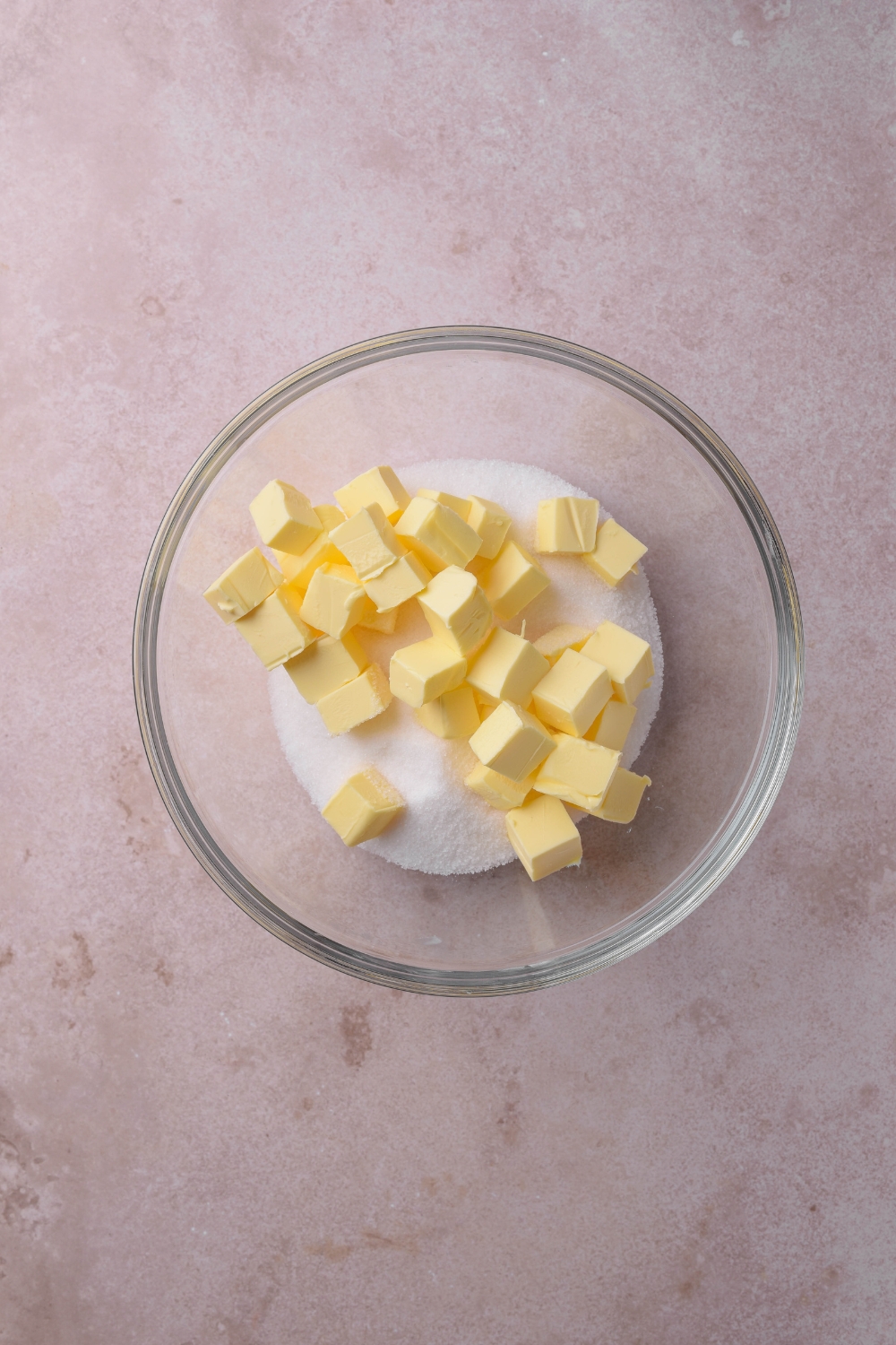 A glass bowl holds cubes of butter and white sugar.