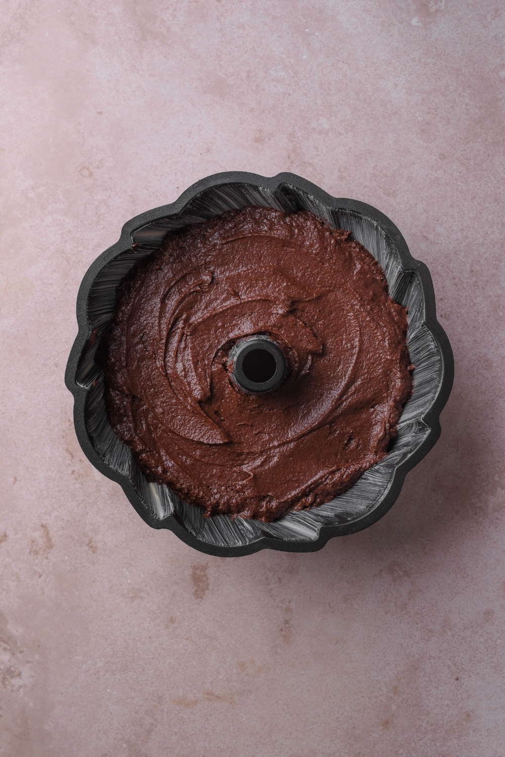 A black bundt pan holds chocolate pound cake batter.