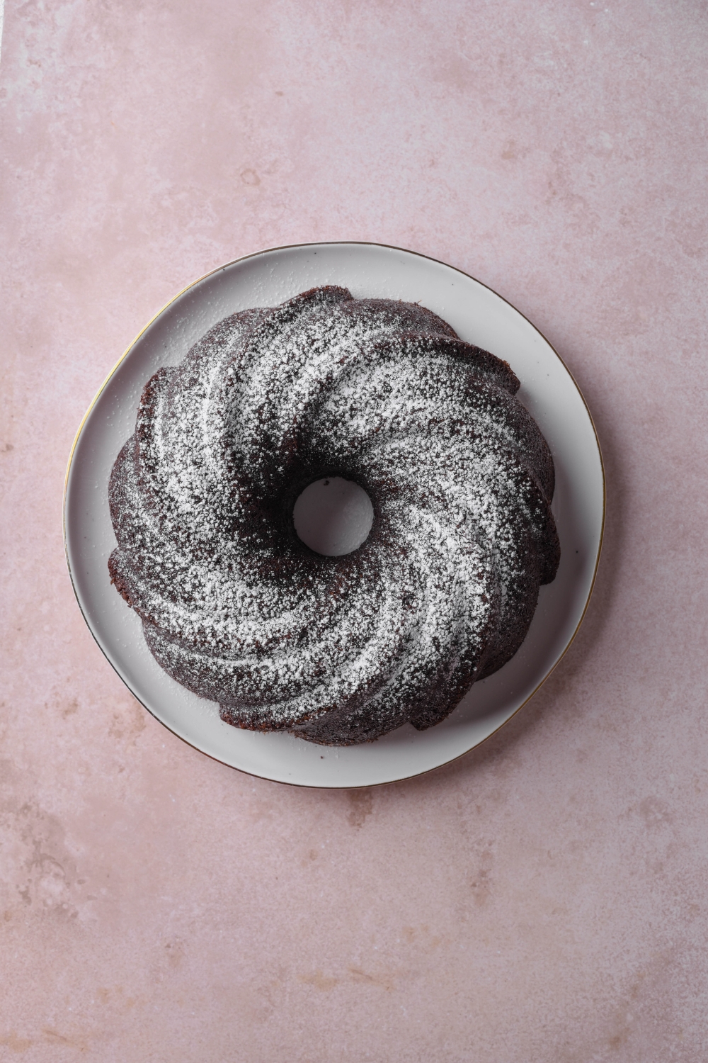A sugar dusted chocolate pound cake sits on a white serving plate.