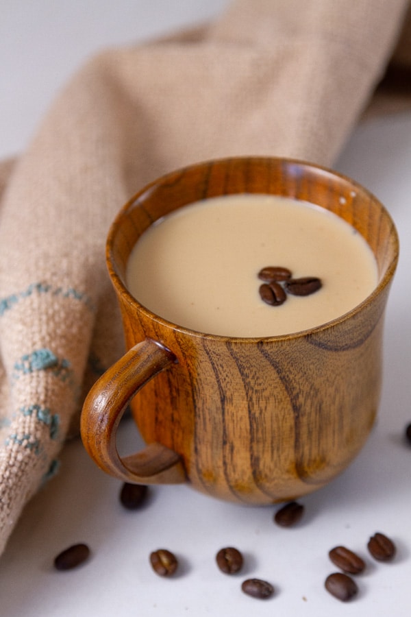 a wooden mug filled with a warm chai hot toddy, coffee beans around it and a brown cloth napkin.