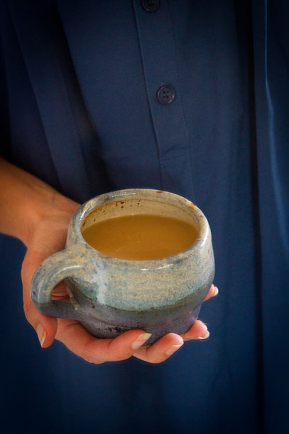 a hand holding a blue mug filled with a warm chai drink.