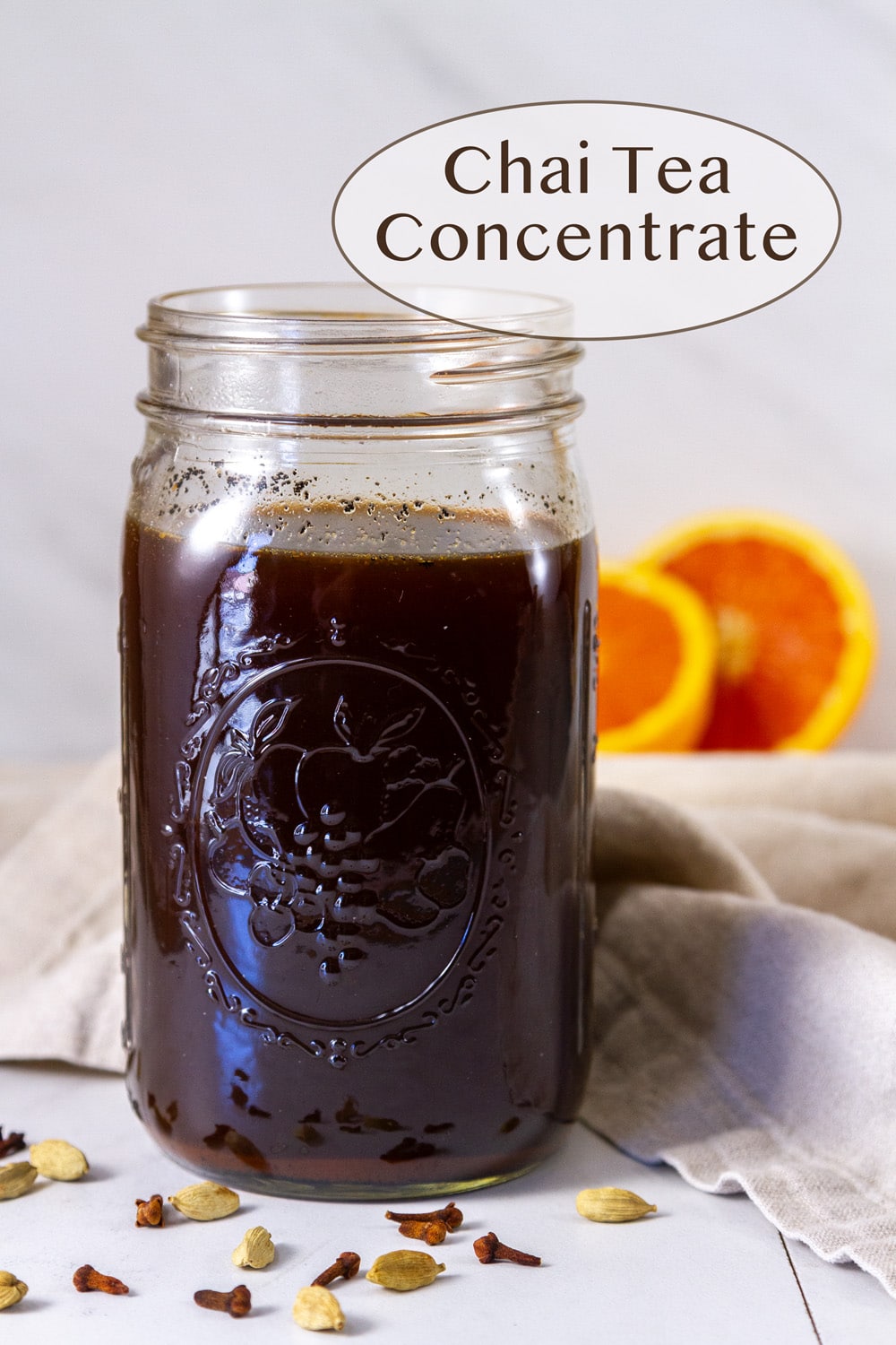 a large mason jar filled with chai concentrate drink and some sliced oranges in the background.