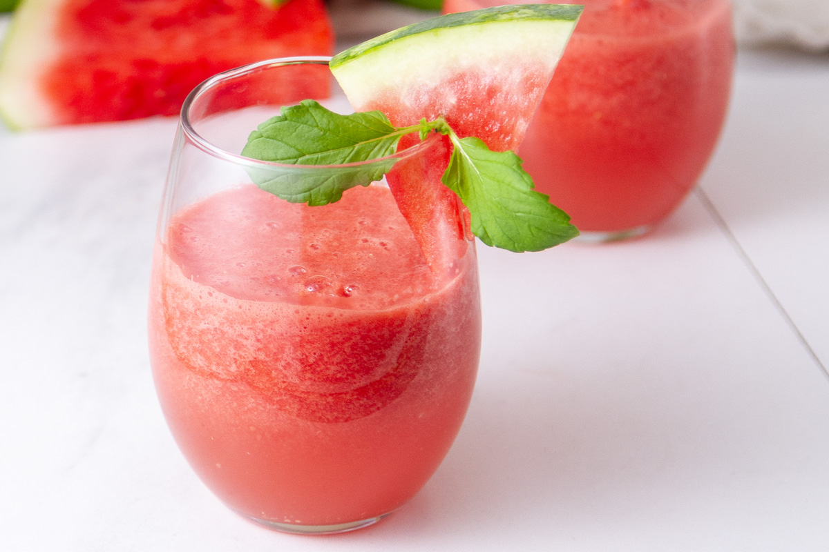 a glass filled with watermelon drink and garnished with a slice of watermelon.