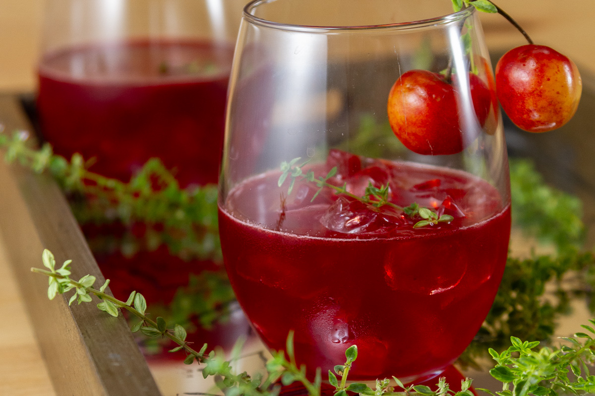 two glasses of cherry scotch drinks garnished with fresh cherries.
