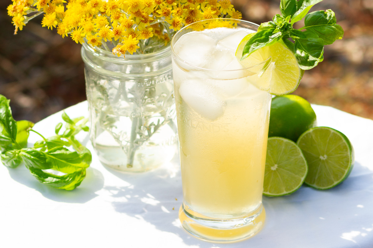a glass of iced green tea next to cut limes and a vase of yellow flowers.