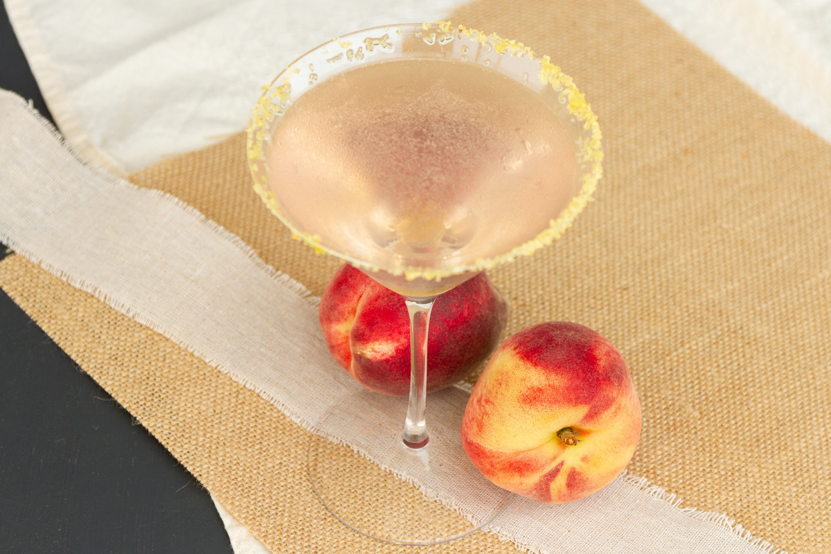 a martini glass filled with peach coconut drink and peaches at the bottom of the glass.