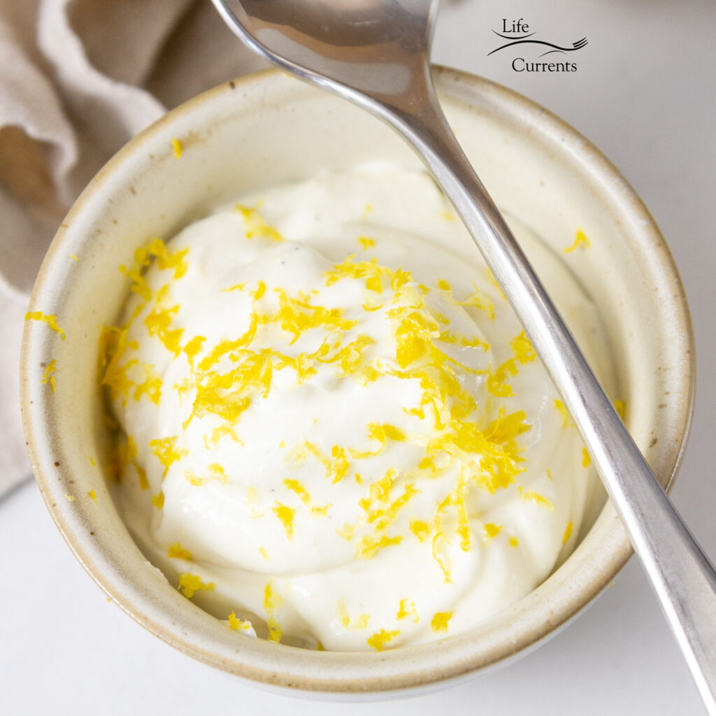 square crop of a bowl of lemon cottage cheese pudding with a spoon on the side.
